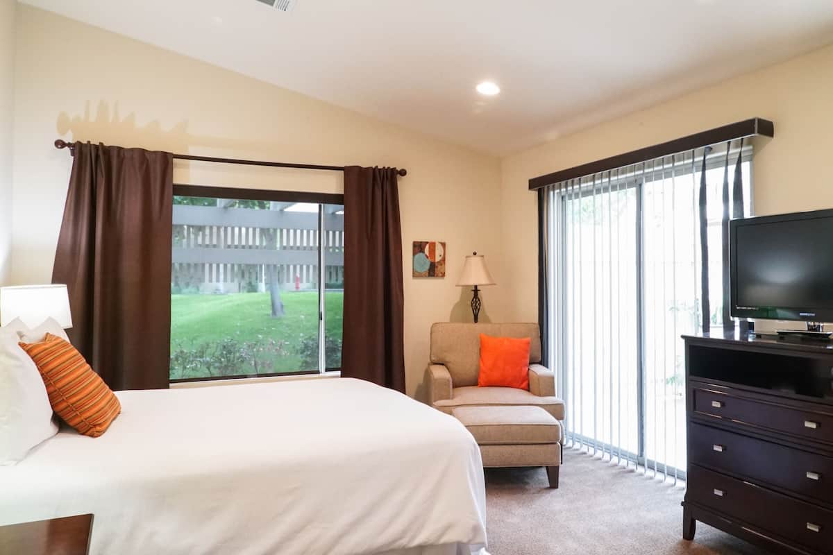 A hotel room with a bed, a chair, a TV, and a window with curtains.