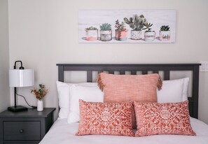 A neatly made bed with white and patterned pillows, a dark headboard, and a nightstand with a lamp and a vase of flowers. - The Villas at Emerald Desert RV Resort (Palm Desert)