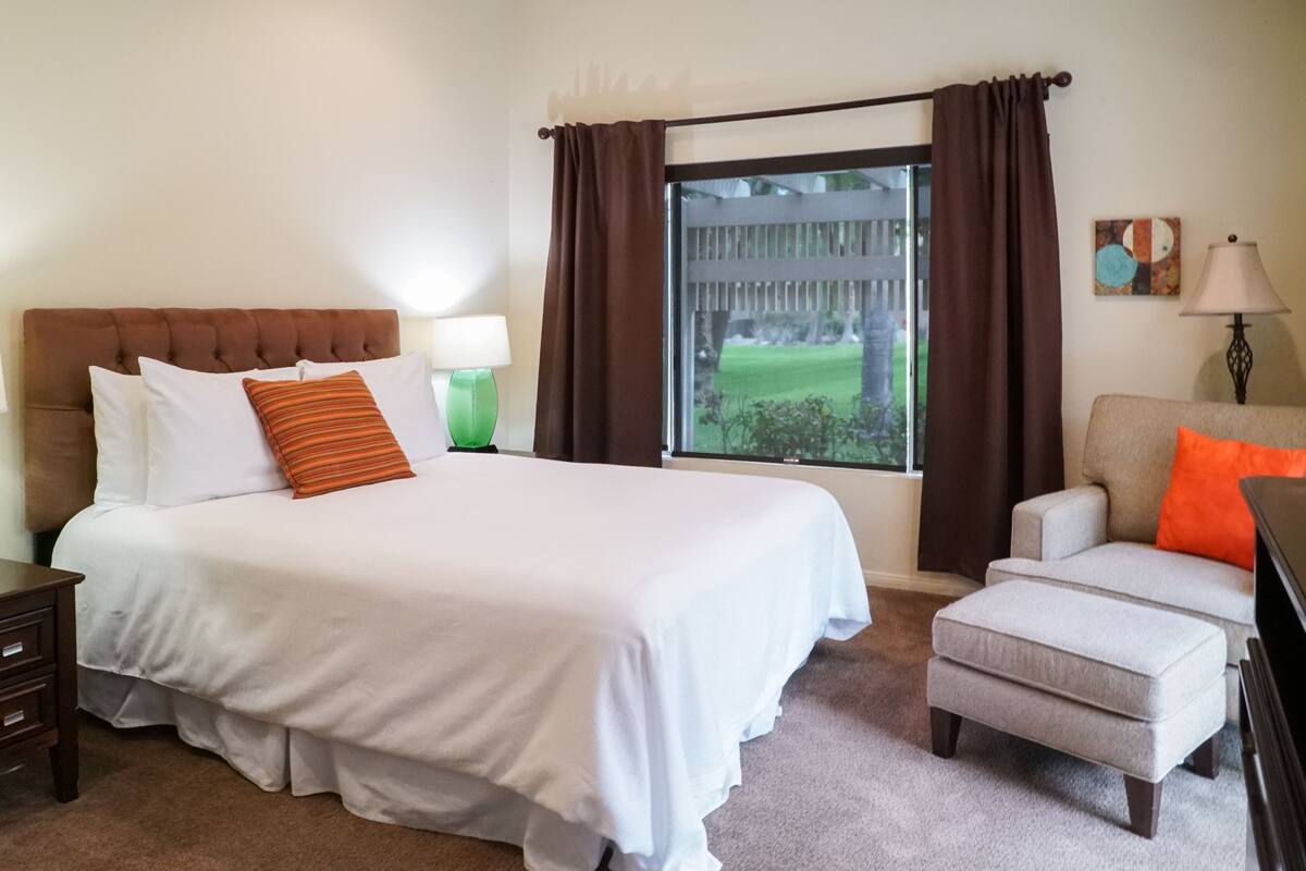 A hotel room with a large bed, a chair, a nightstand, and a window with curtains.
