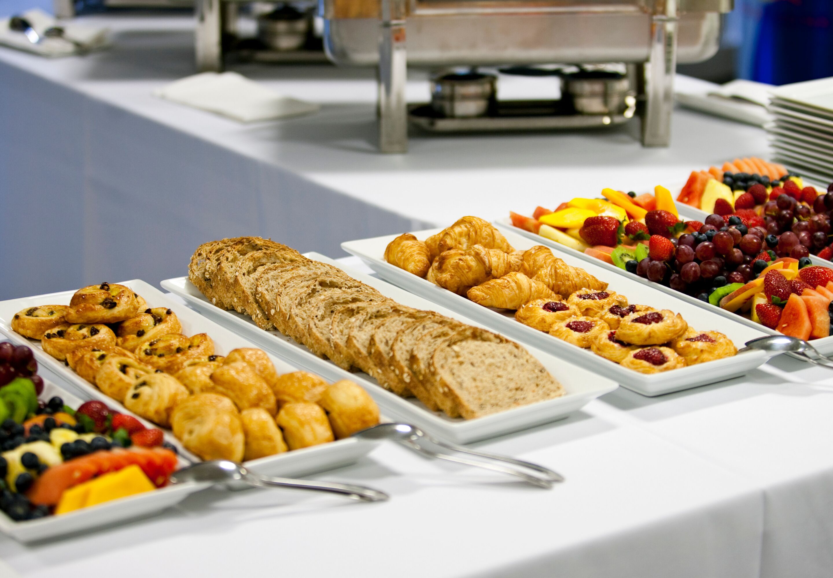 A buffet table with various food items including pastries, fruits, and a large loaf of bread.