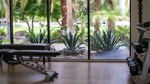 A gym with a bench and dumbbells, large windows with a view of palm trees and greenery. - The Villas at Emerald Desert RV Resort (Palm Desert)