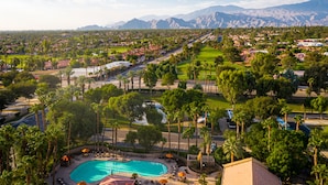 A resort with a swimming pool, palm trees, and a view of mountains. - The Villas at Emerald Desert RV Resort (Palm Desert)