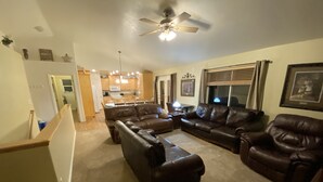 A living room with a brown leather sofa set, a ceiling fan, and a kitchen in the background. - Beautiful home, 8 bedrooms-18 beds-sleeps 30, family friendly (Ammon)