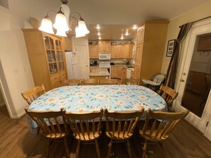 A dining area with a floral tablecloth, wooden chairs, and a kitchen in the background.