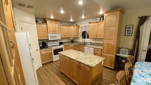 A compact kitchen with wooden cabinets, a central island, a microwave, an oven, and a dishwasher. - Beautiful home, 8 bedrooms-18 beds-sleeps 30, family friendly (Ammon)