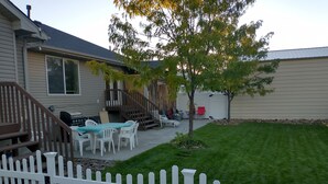 A backyard with a white picket fence, a lawn, a barbecue area, and a covered patio with outdoor furniture. - Beautiful home, 8 bedrooms-18 beds-sleeps 30, family friendly (Ammon)