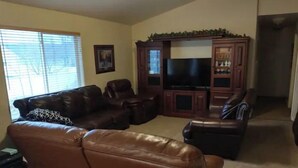 A living room with a brown leather sofa, a television, and wooden cabinets. - Beautiful home, 8 bedrooms-18 beds-sleeps 30, family friendly (Ammon)
