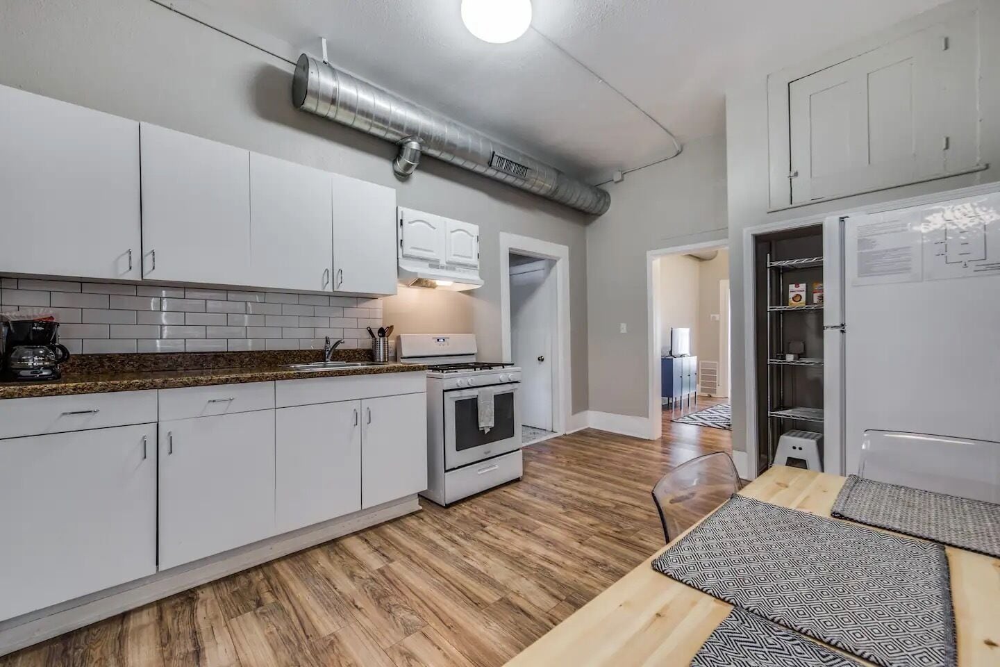 A modern kitchen with white cabinets, a stainless steel range hood, a built-in oven, and a wooden countertop.