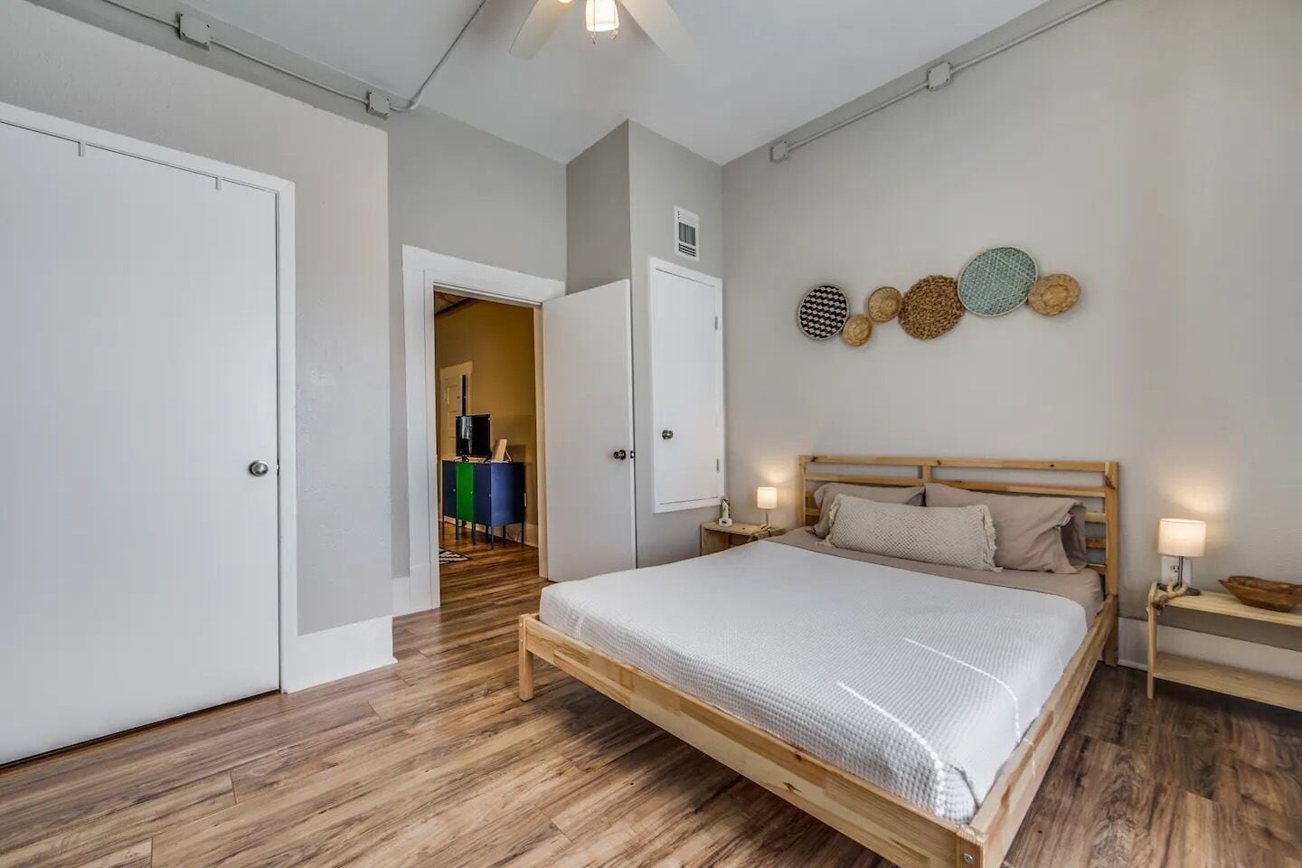 A bedroom with a wooden bed, a wardrobe, and a dresser. There are wall-mounted lights and a door leading to another room.