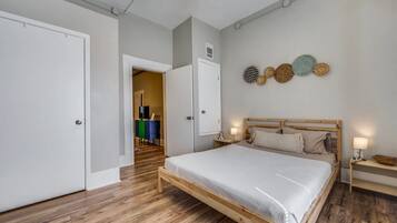 A bedroom with a wooden bed, a wardrobe, and a dresser. There are wall-mounted lights and a door leading to another room.