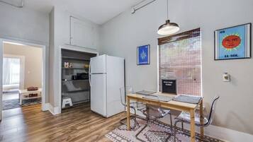 A compact kitchen with a refrigerator, a dining table with chairs, and a window with blinds.