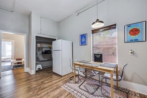 A compact kitchen with a refrigerator, a dining table with chairs, and a window with blinds.