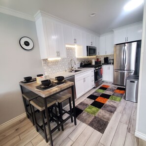 A modern kitchen with white cabinets, a wooden dining table, and a colorful rug. - Modern Residence in Torrance 15 mins from LAX (Torrance)