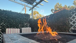 Une terrasse en pierre avec un foyer, un coussin à rayures et une clôture à treillis.
