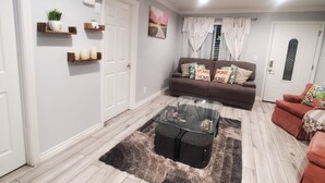 Un salon avec un canapé, une table basse et un tapis. Il y a une porte et un appareil de climatisation sur le mur.