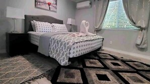 Une chambre à coucher avec un lit, des tables de chevet, un tapis, un tableau et une fenêtre avec des rideaux.