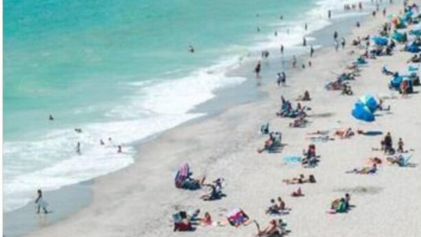 Une plage bondée où les gens se prélassent au soleil et se baignent.