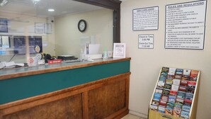 A hotel reception desk with a clock, a 'No Smoking' sign, a 'Check-In Time 3:00 PM' sign, a 'Check-Out Time 11:00 AM' sign, and a 'No Pets Allowed' sign. - James River Inn & Suites (Newport News)