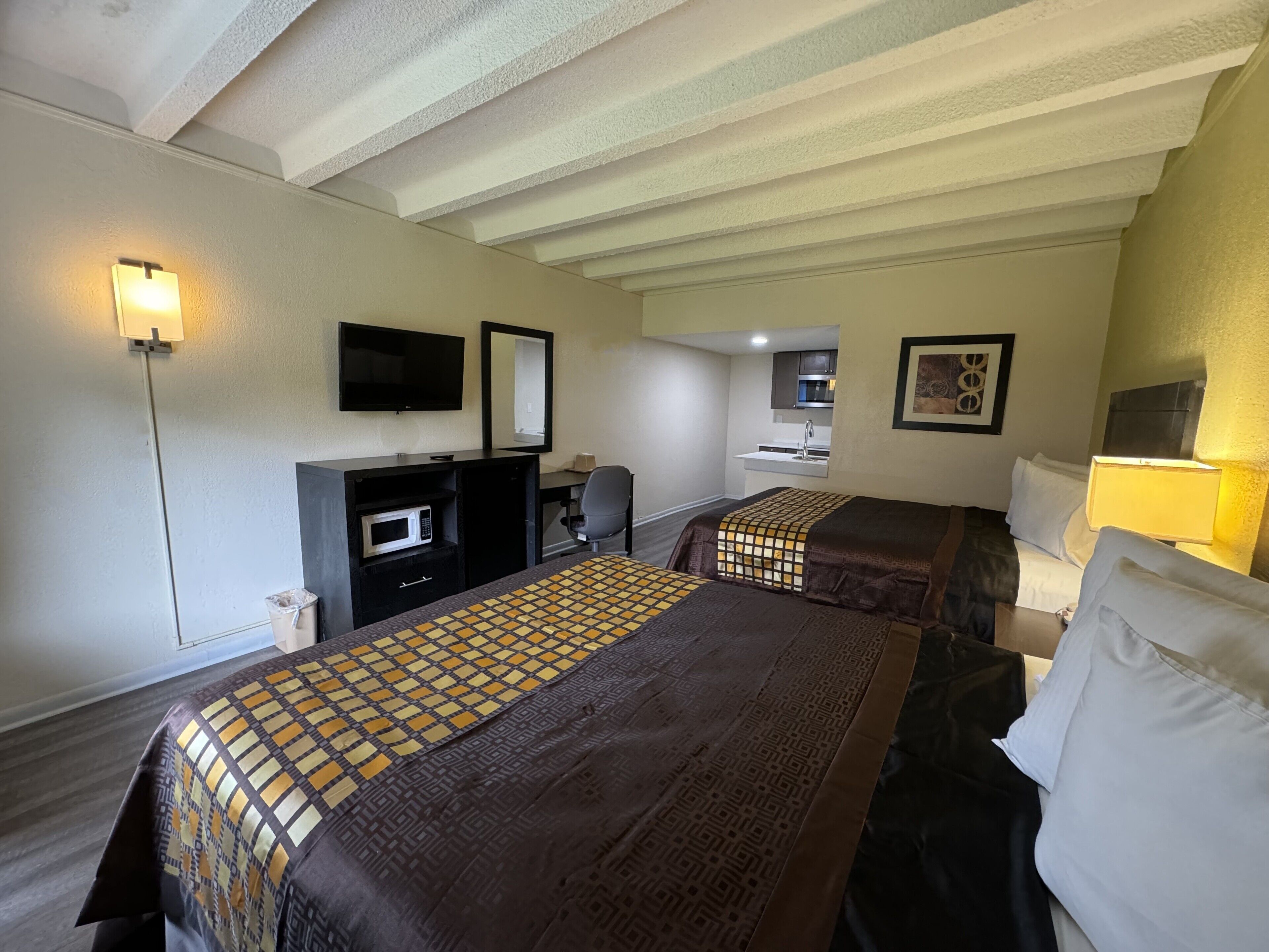 A hotel room with two beds, a desk, a microwave, a TV, and a small kitchenette.