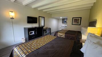 A hotel room with two beds, a desk, a microwave, a TV, and a small kitchenette.