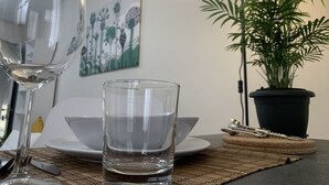 Een eettafel met een wijnglas, een waterglas en een schaal. Er staat een potplant en aan de muur hangt een schilderij.