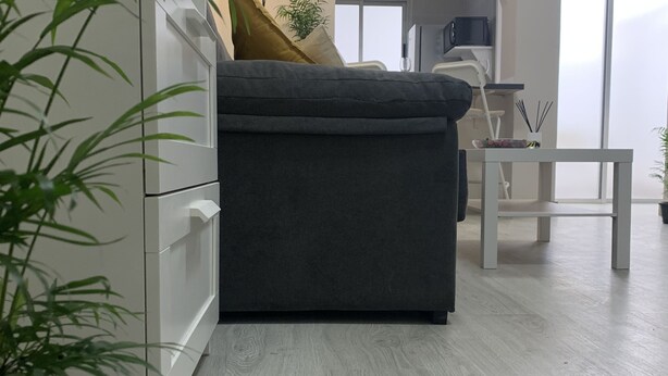 Een moderne woonkamer met een grijze bank, witte kasten en een houten vloer.