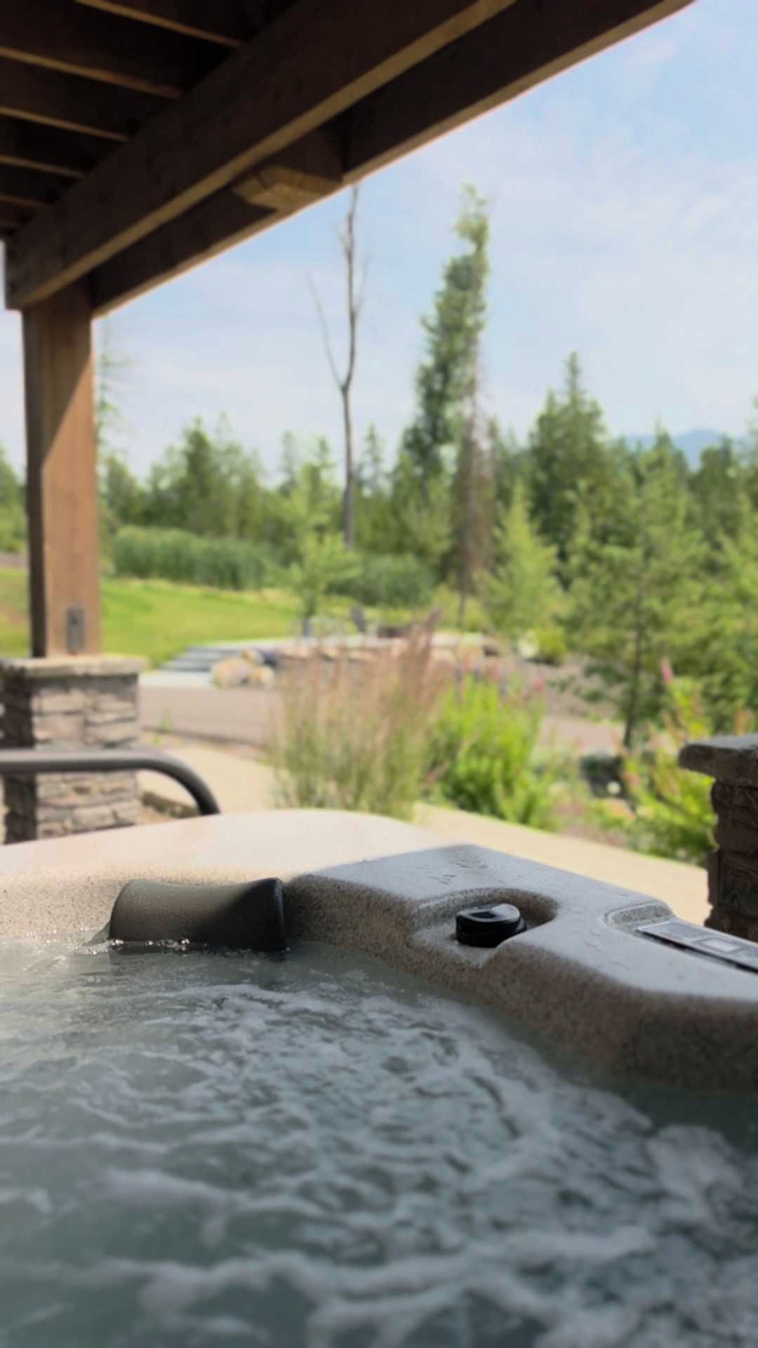 Ein Whirlpool unter einer Holzpergola mit Blick auf einen angelegten Garten und Bäume.