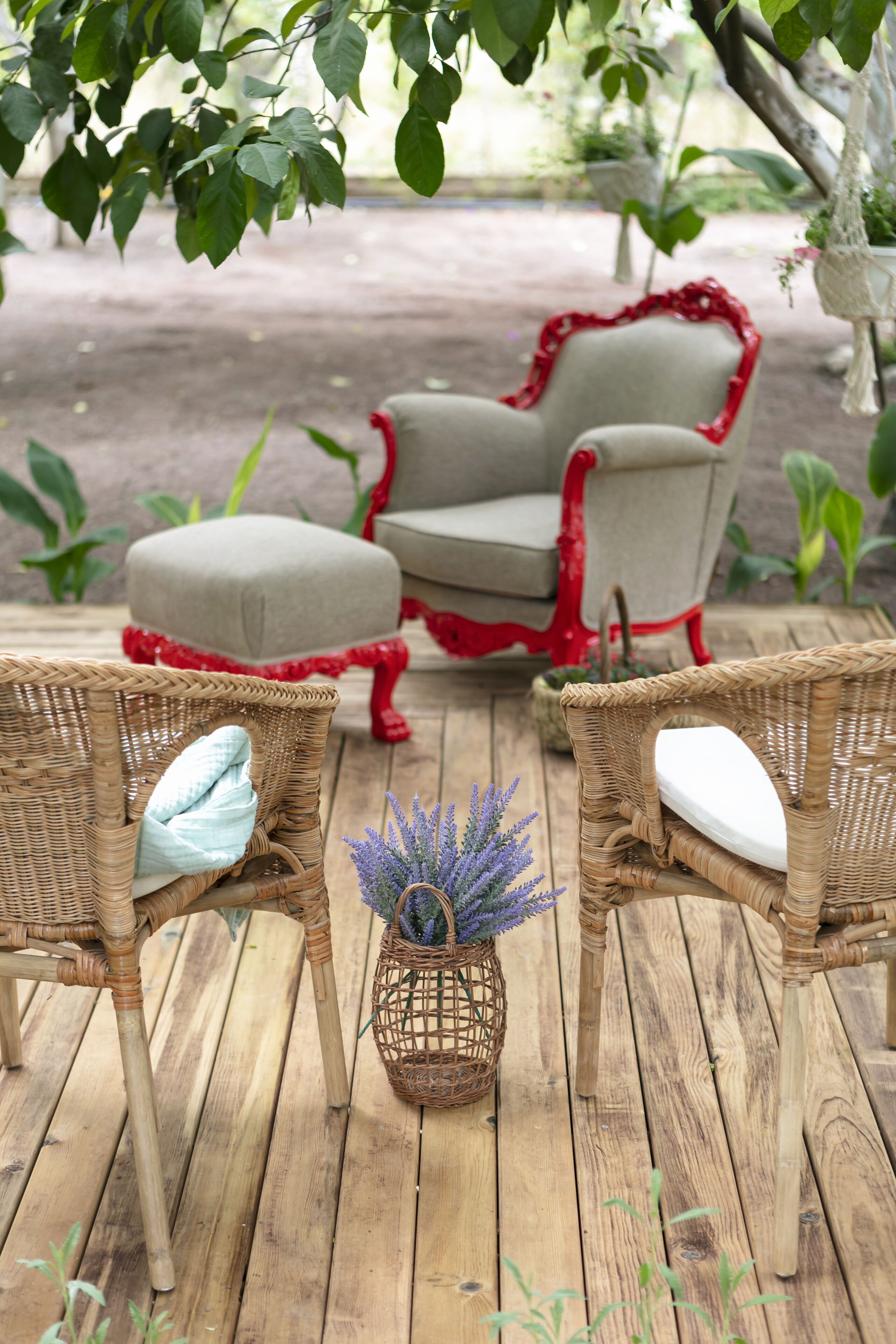 A wooden deck with wicker chairs and a cushioned bench, surrounded by greenery and potted plants.