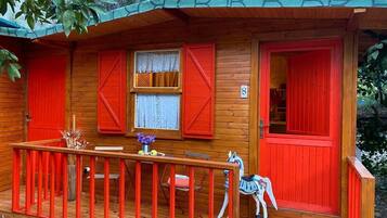 A wooden cabin with red doors and shutters, a small porch with a railing, and a decorative horse figure.