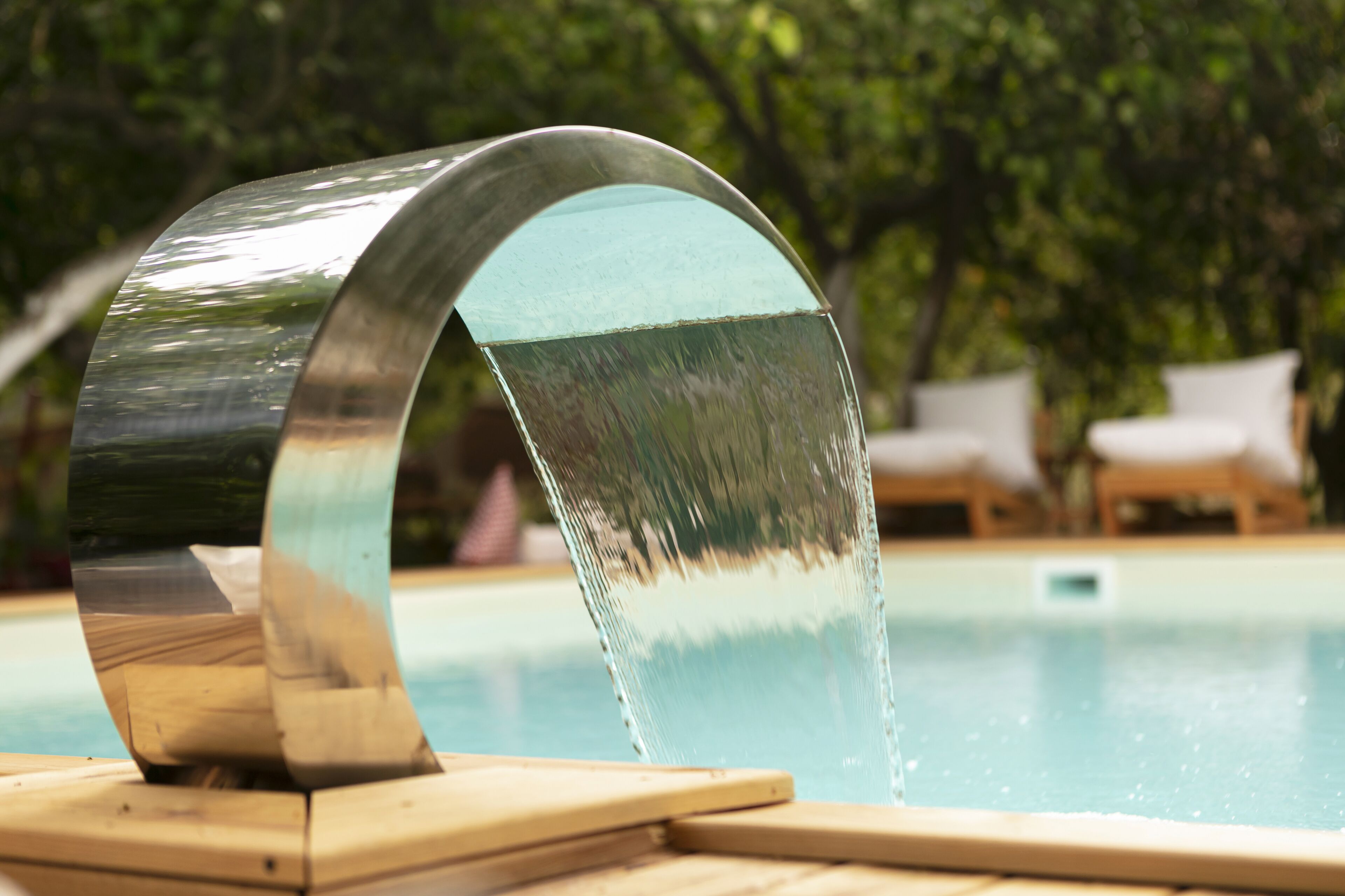 Una piscina moderna con un elemento acuático único y sillones de descanso al fondo.