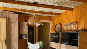 Interior de madera con una mesa y sillas de comedor, una lámpara colgante y estantes de madera con frascos de vidrio.