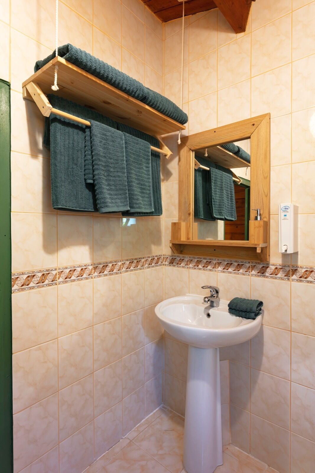 Un baño con un toallero de madera que sostiene dos toallas, un lavabo blanco y un espejo con marco de madera.