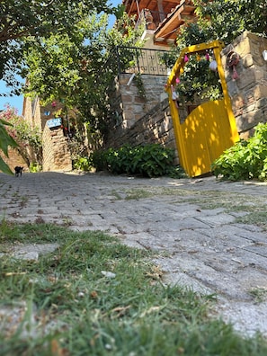 Ein Kopfsteinpflasterweg führt zu einem Steinhaus mit einem gelben Tor.