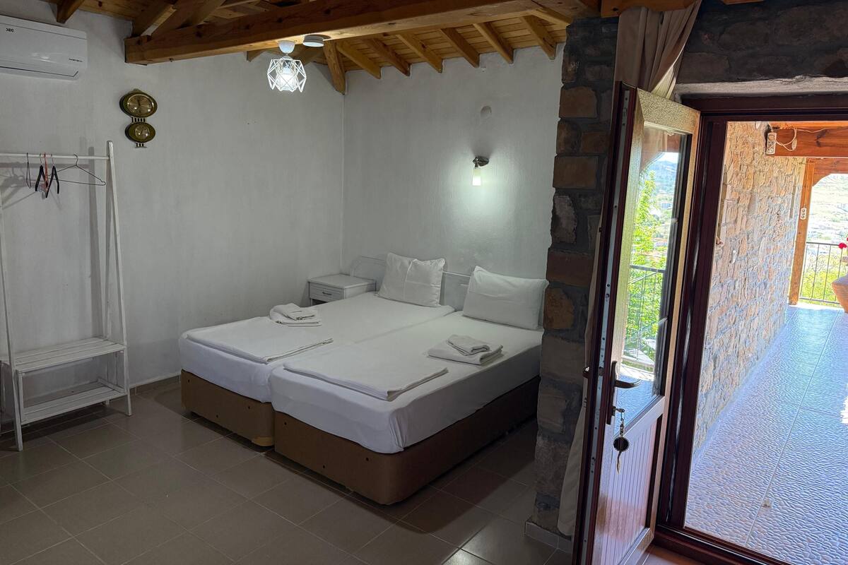 Un dormitorio con techo de madera, una cama con ropa de cama blanca, una mesita de noche pequeña y un reloj en la pared.