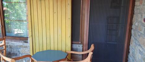 Un patio couvert avec un mur en pierre, une table en bois agrémentée de coussins violets et un paravent jaune.