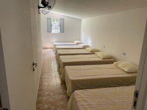 A corridor with multiple beds lined up against the wall, a fan mounted on the wall, and a window with shutters. - Beautiful farmhouse with a pool, barbecue, comfort, and fun in Ibiúna. (Ibiuna)