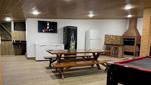 Una cuina moderna amb taula de fusta, nevera, nevera Heineken, forn de rajola i un televisor penjat a la paret.