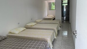 Habitació d'hotel amb tres llits, una finestra petita i una porta que dona a un bany.
