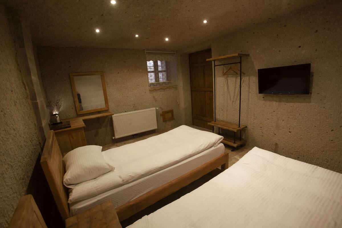 Quarto com duas camas de madeira, um guarda-roupa de madeira, uma mesinha, um espelho, uma janela e uma televisão.