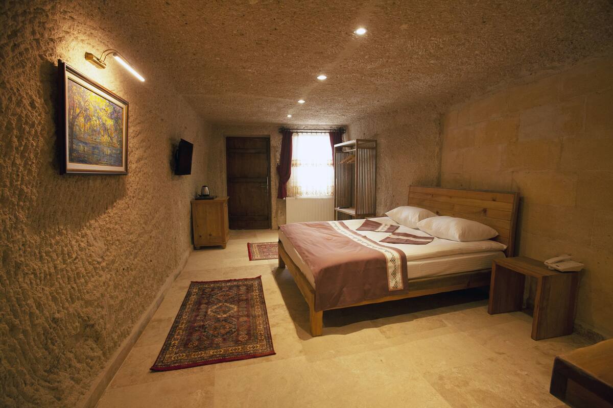 Quarto com cama de madeira, mesa de cabeceira, um quadro emoldurado na parede e janela com cortinas.