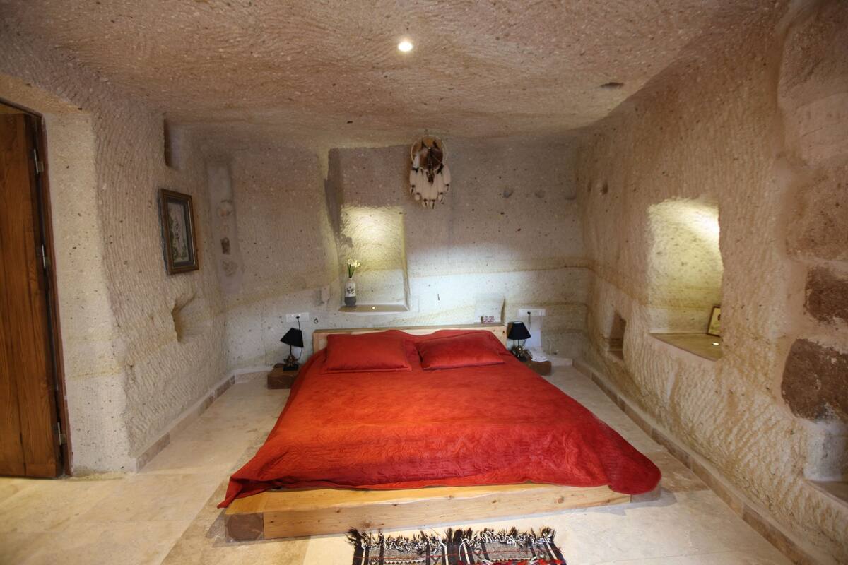 Quarto com uma cama grande, cabeceira de madeira, paredes de pedra e porta de madeira.