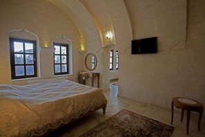 A bedroom with a large bed, two windows, a television on the wall, and a small table.