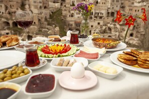 A table set with various dishes, a glass of red wine, and a vase of flowers against a backdrop of historic buildings.