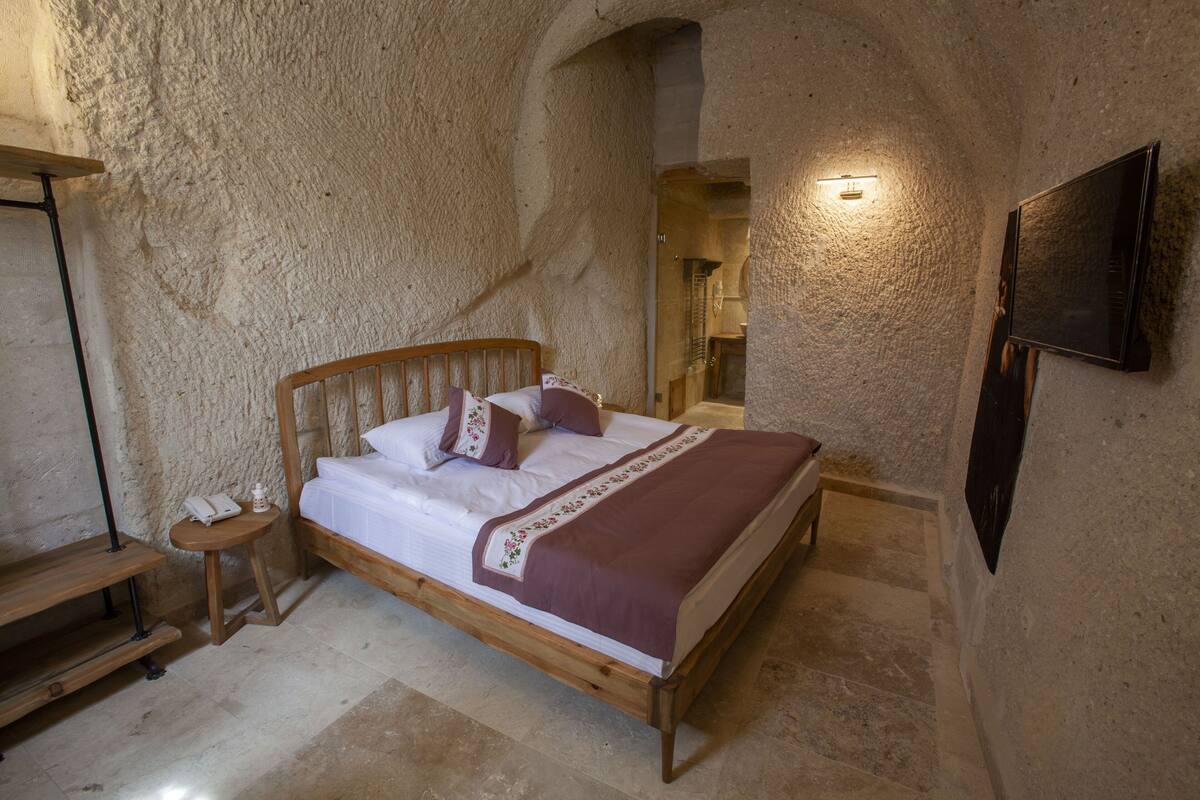 Quarto com cama de madeira, mesa de cabeceira e televisão fixada na parede.