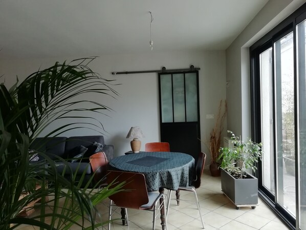 A modern room with a dining table, chairs, a sofa, a potted plant, and a sliding glass door leading to a balcony.