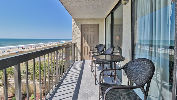 Ein Balkon mit Blick auf den Strand, eine Tür und zwei Korbstühle.
