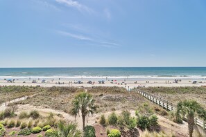 Une plage avec une promenade en bois, des dunes de sable et une végétation clairsemée.
