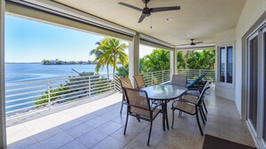 Een ruim balkon met een tafel en stoelen, met uitzicht op een wateroppervlak en palmbomen.