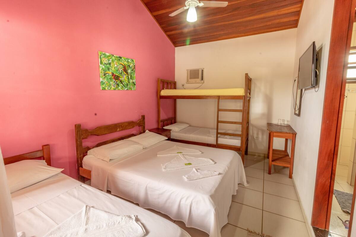 Une chambre avec deux lits simples, un lit superposé, un ventilateur de plafond en bois, une télévision et une petite table.