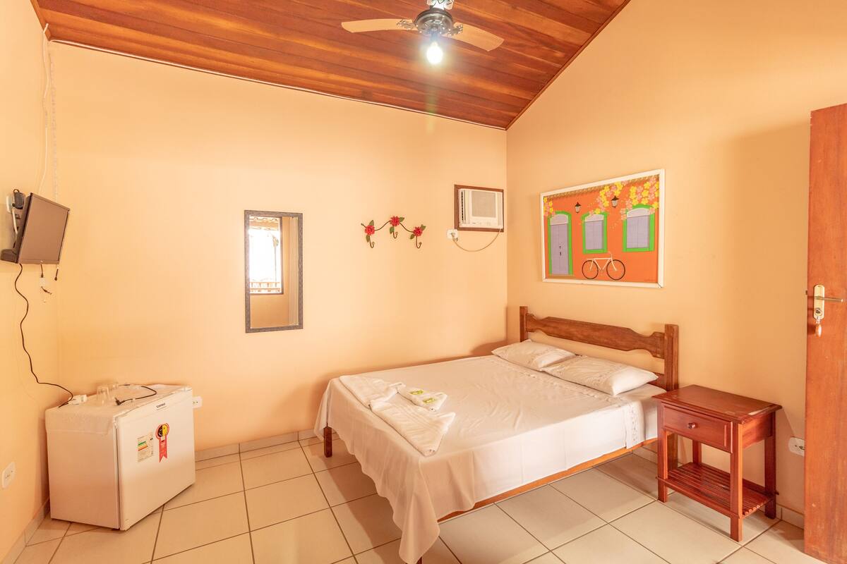 Une chambre à coucher comprenant un lit, une table de chevet, un climatiseur mural et un réfrigérateur.